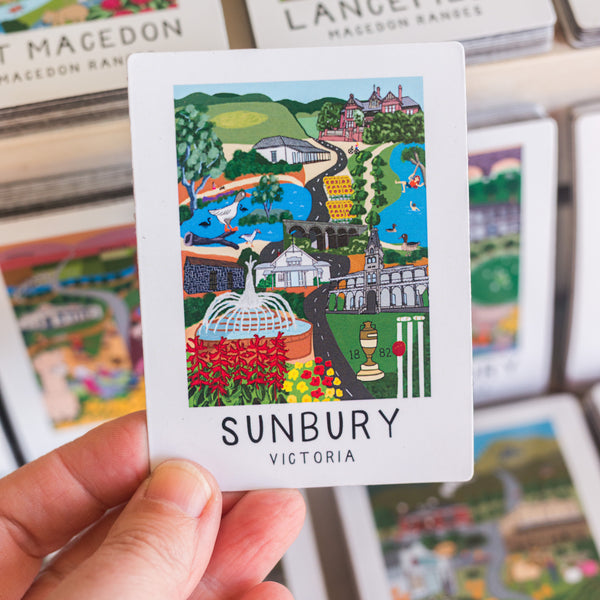 Card with a colorful illustration magnet of Sunbury, Victoria held by a hand, with other similar cards in the background.