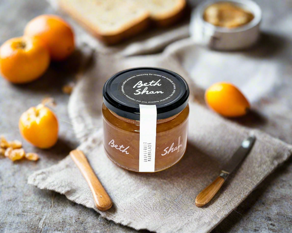 a jar of grapefruit marmalade on a kitchen table surrounded by toast and fruit