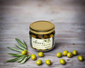 a jar of green table olives grown in the Macedon Ranges on a table with some green olives
