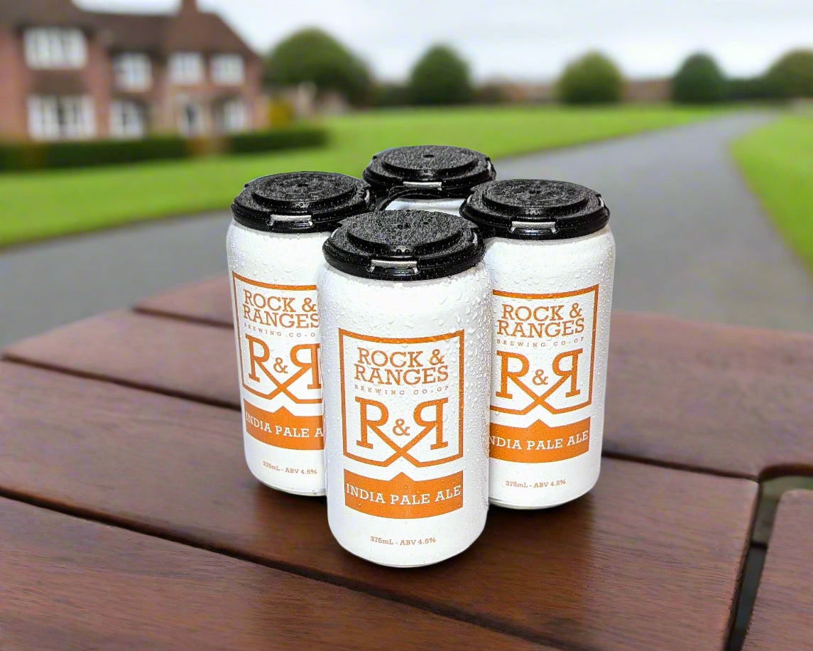 four cans of Indian pale ale on a table in country setting