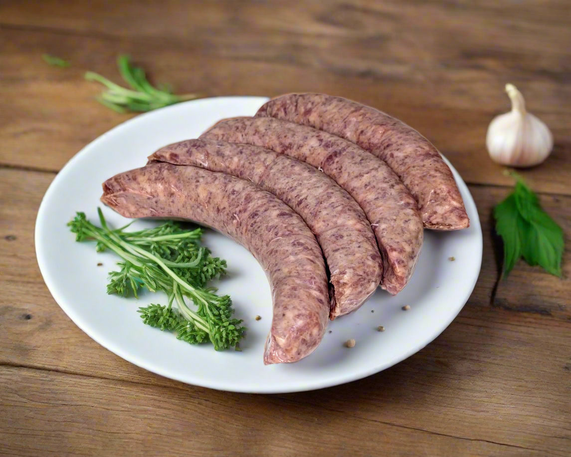 black pepper and garlic sausages made in the Macedon Ranges on a plate with fresh herbs and garlic in the background