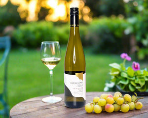 a bottle of Macedon Ranges white wine on a table in the garden with glass of wine and grapes