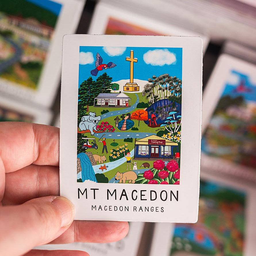 Hand holding a magnet with 'MT Macedon Macedon Ranges' design among other cards.