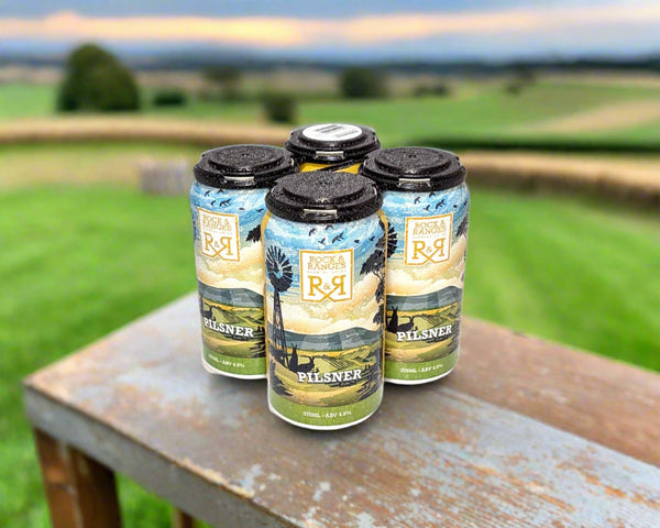 four cans of Macedon Ranges Pilsner beer on a bench in farm setting