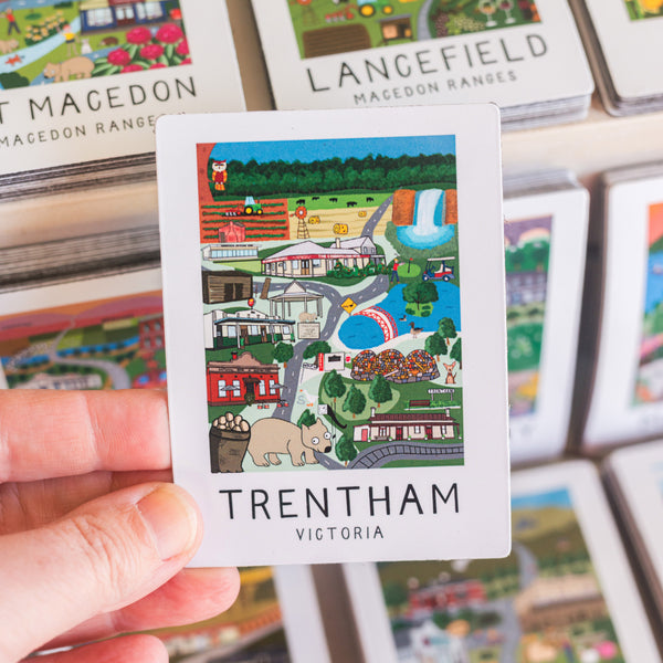 Card with a colorful illustration magnet of Trentham, Victoria held by a hand, with more cards in the background.
