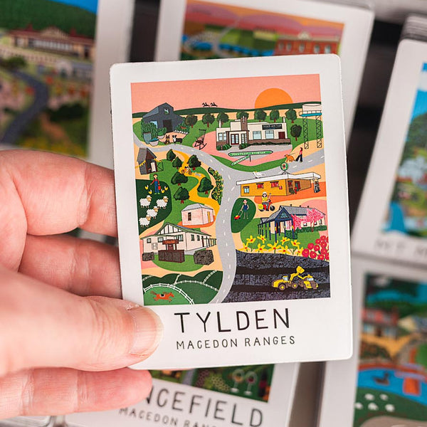 Hand holding a miniature map magnet labeled 'Tylden Macedon Ranges' with other similar cards in the background.